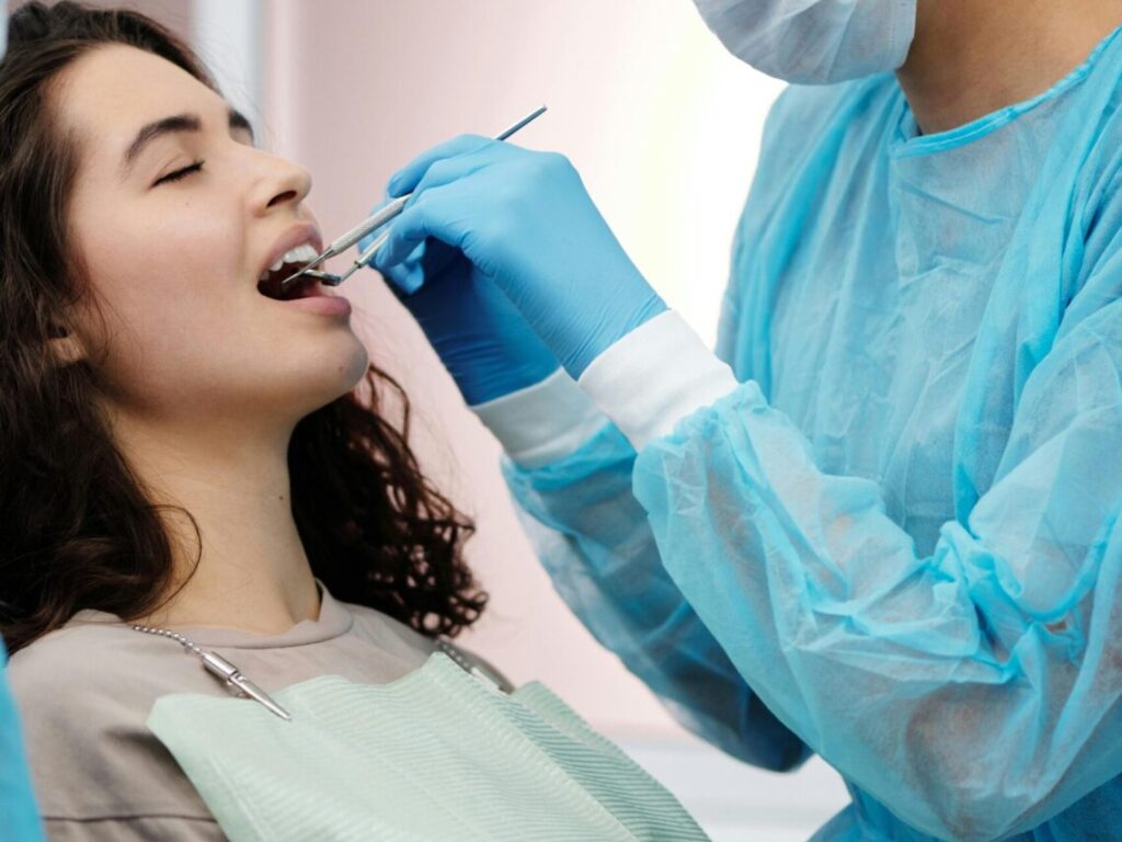 Dentist in protective gear examining a woman's teeth during a dental clinic visit.